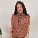 Woman standing in a room with decorative elements like a vase, plant, and small table.