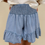 Kira Smocked Shorts in light denim blue with smocked waist and tiered ruffle hem — Paper Doll