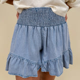 Kira Smocked Shorts in light denim blue with smocked waist and tiered ruffle hem — Paper Doll