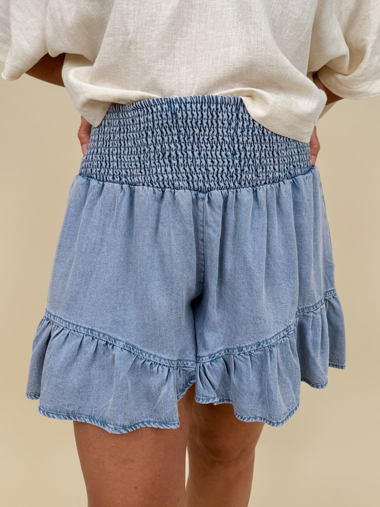 Kira Smocked Shorts in light denim blue with smocked waist and tiered ruffle hem — Paper Doll