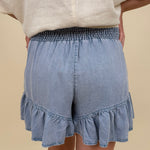 Kira Smocked Shorts in light denim blue with smocked waist and tiered ruffle hem — Paper Doll