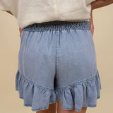 Kira Smocked Shorts in light denim blue with smocked waist and tiered ruffle hem — Paper Doll