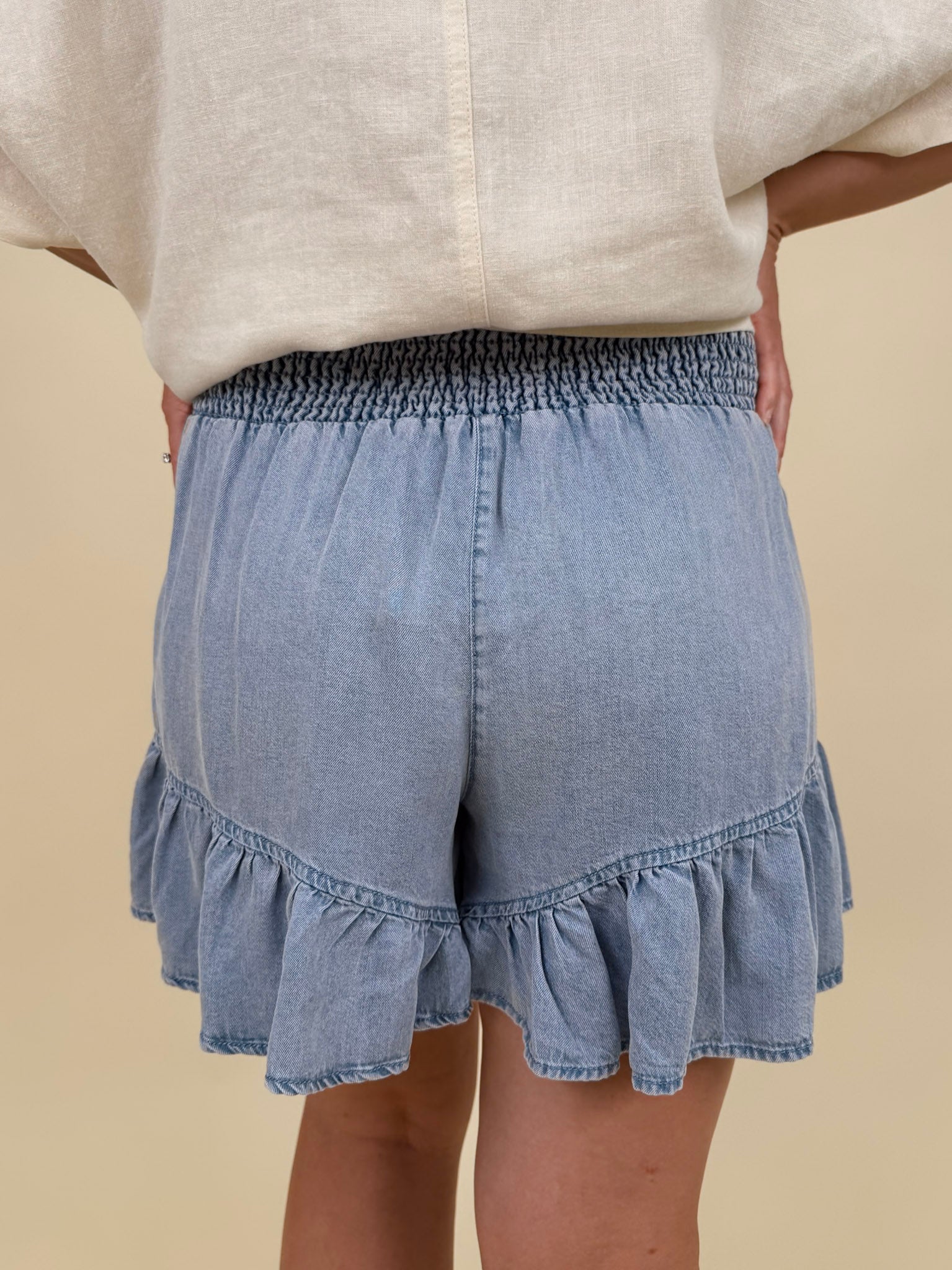 Kira Smocked Shorts in light denim blue with smocked waist and tiered ruffle hem — Paper Doll