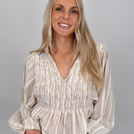 Woman wearing neutral striped Boardwalk Blouse with smocked bodice, collared V-neckline, billowy long sleeves, and relaxed flowing fit