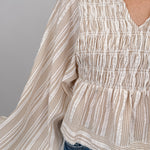 Woman wearing neutral striped Boardwalk Blouse with smocked bodice, collared V-neckline, billowy long sleeves, and relaxed flowing fit