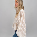 Woman wearing neutral striped Boardwalk Blouse with smocked bodice, collared V-neckline, billowy long sleeves, and relaxed flowing fit