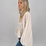 Woman wearing neutral striped Boardwalk Blouse with smocked bodice, collared V-neckline, billowy long sleeves, and relaxed flowing fit