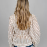 Woman wearing neutral striped Boardwalk Blouse with smocked bodice, collared V-neckline, billowy long sleeves, and relaxed flowing fit