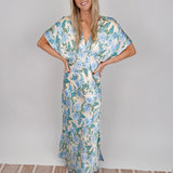 Woman wearing cream Marigold Maxi Dress with blue hydrangea floral print, twisted front waist detail, kimono sleeves, and V-neckline