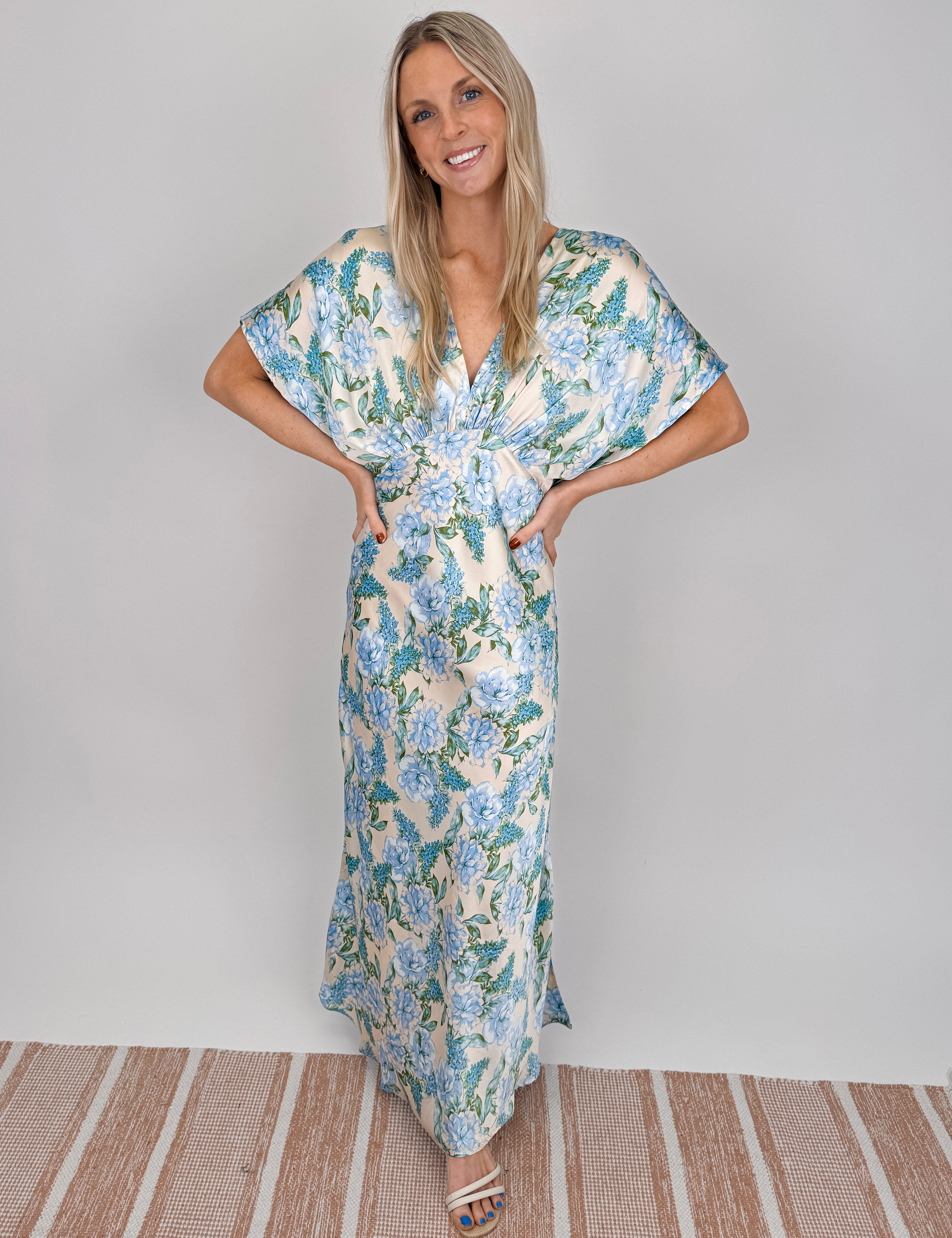 Woman wearing cream Marigold Maxi Dress with blue hydrangea floral print, twisted front waist detail, kimono sleeves, and V-neckline