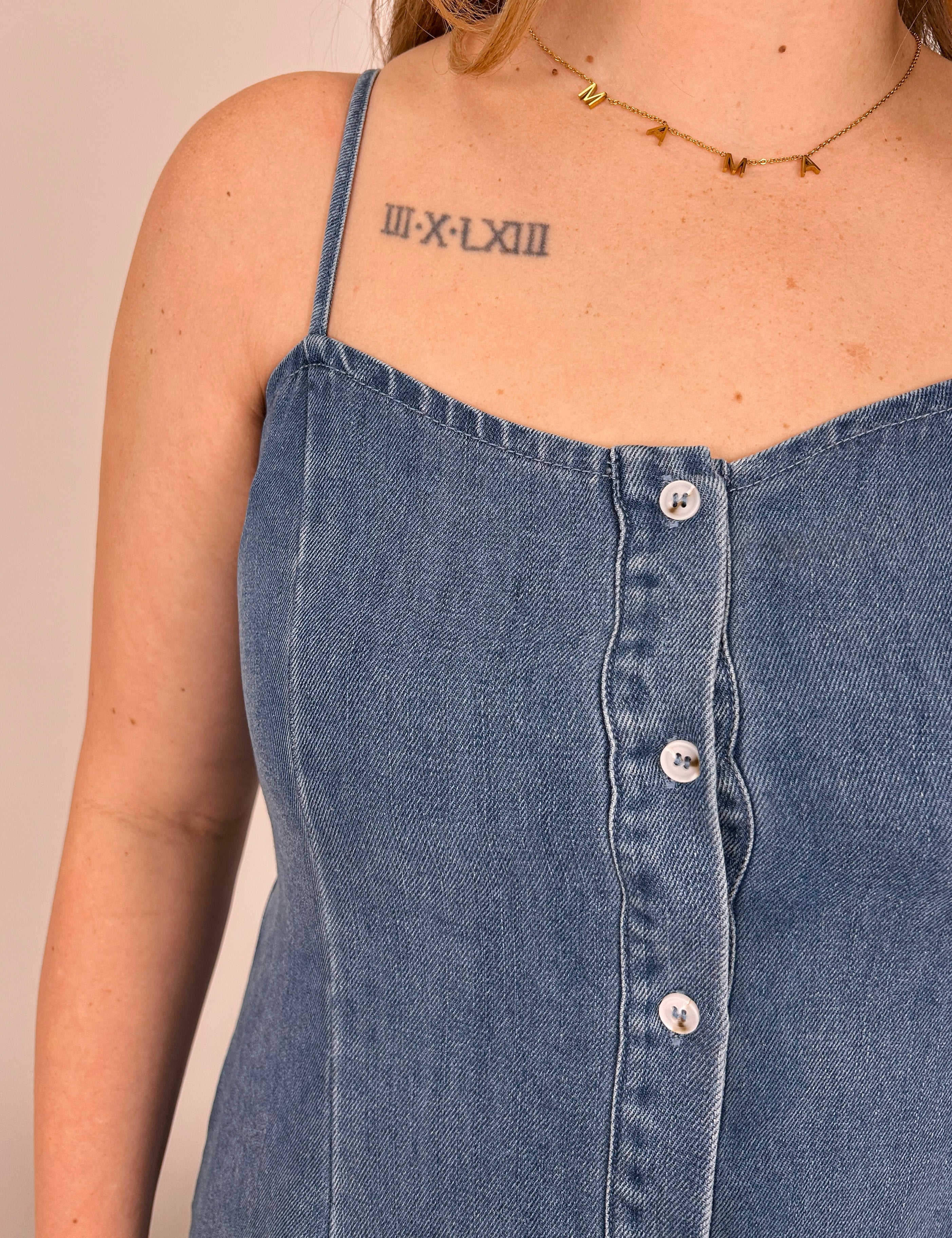 Close-up of a person wearing a blue denim dress with buttons on a beige background