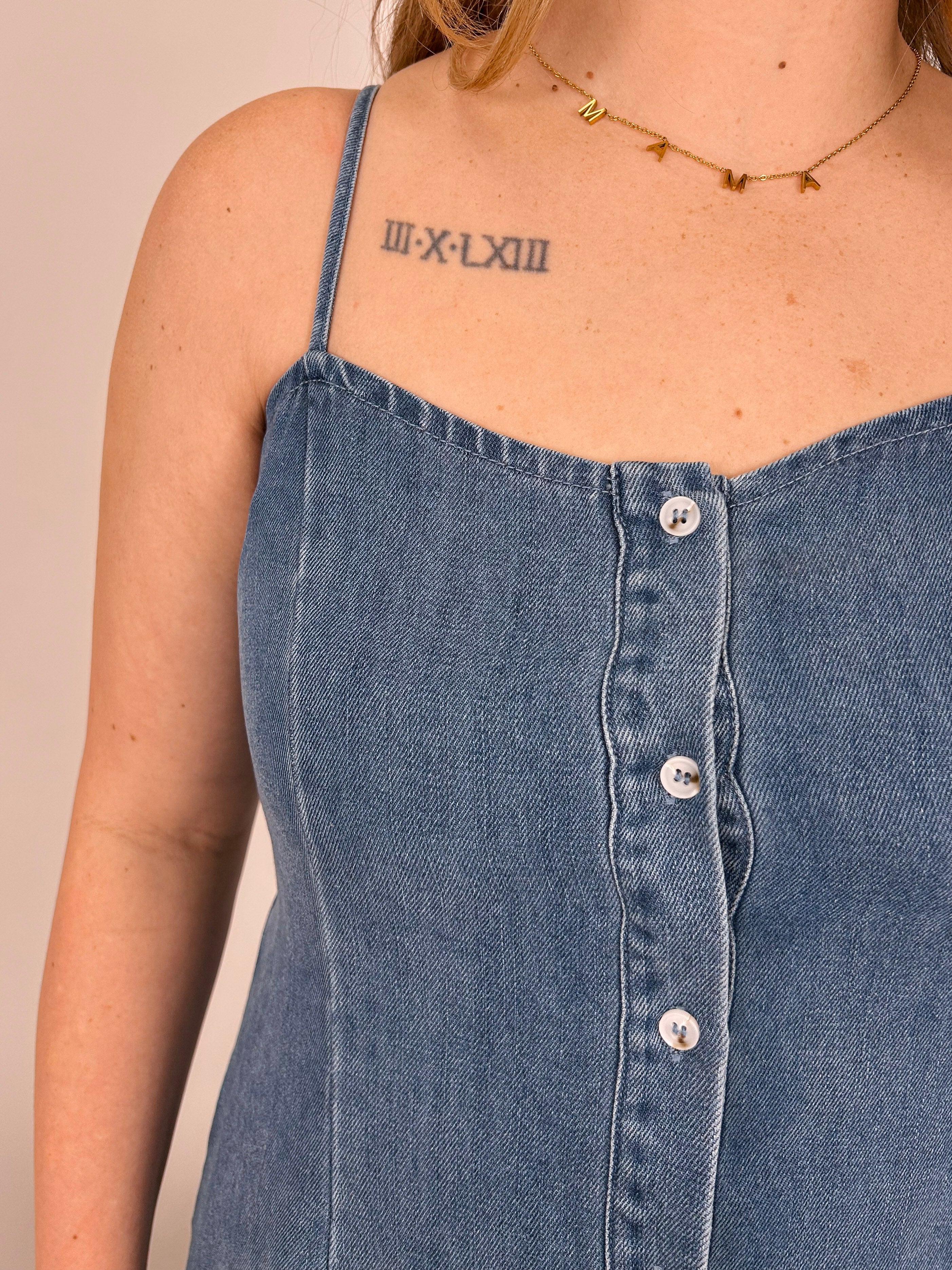 Close-up of a person wearing a blue denim dress with buttons on a beige background