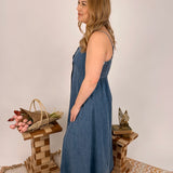 Woman wearing a blue dress standing in a room with wooden furniture and decorative items.