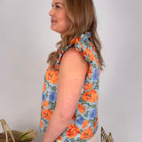 Woman wearing a sleeveless floral top with orange and blue flowers on a plain background