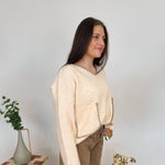 Woman in a beige sweater and brown pants standing in a room with decorative elements.