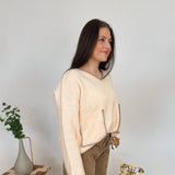 Woman in a beige sweater and brown pants standing in a room with decorative elements.