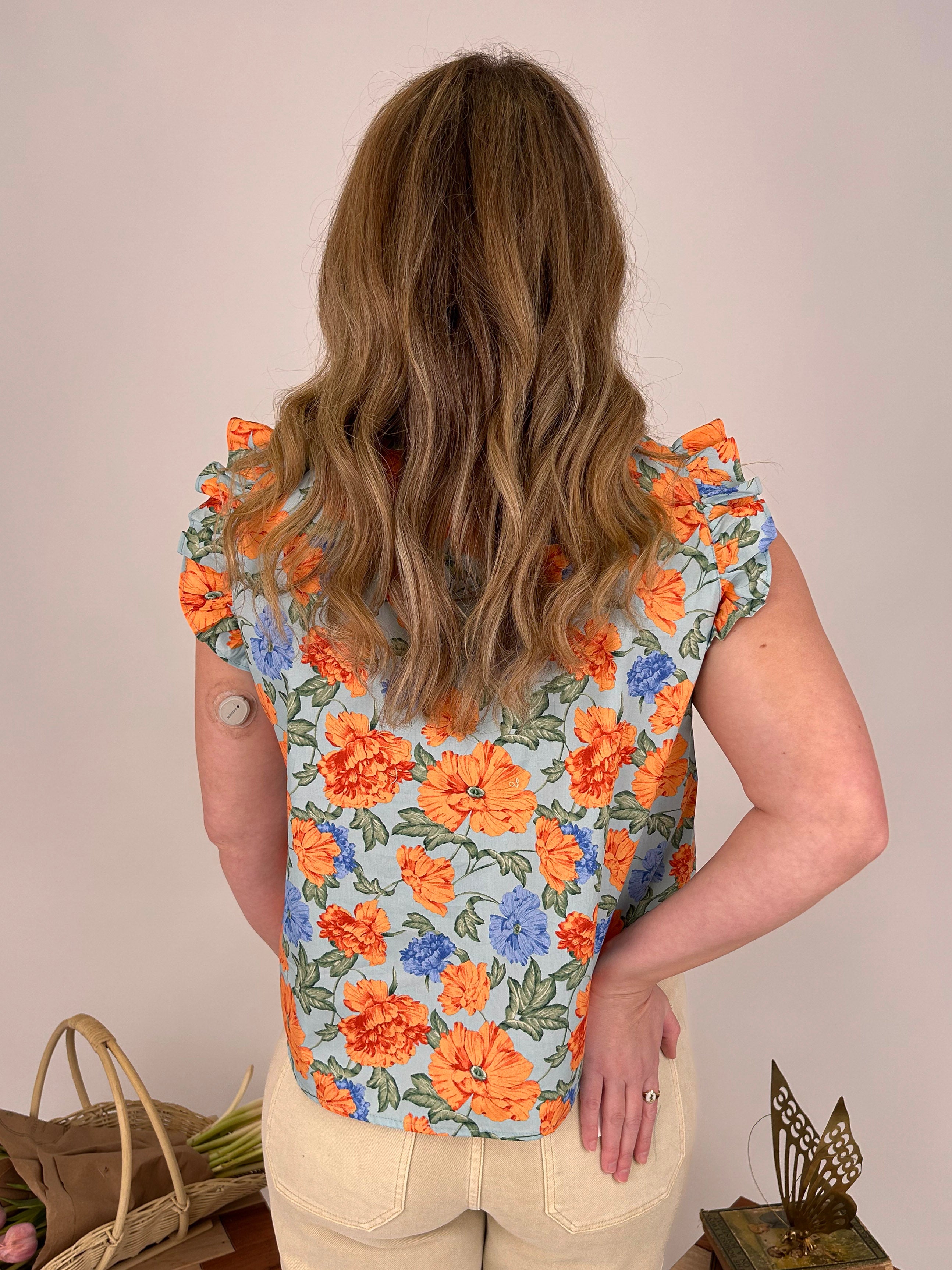 Person wearing a floral sleeveless top with orange and blue flowers on a plain background