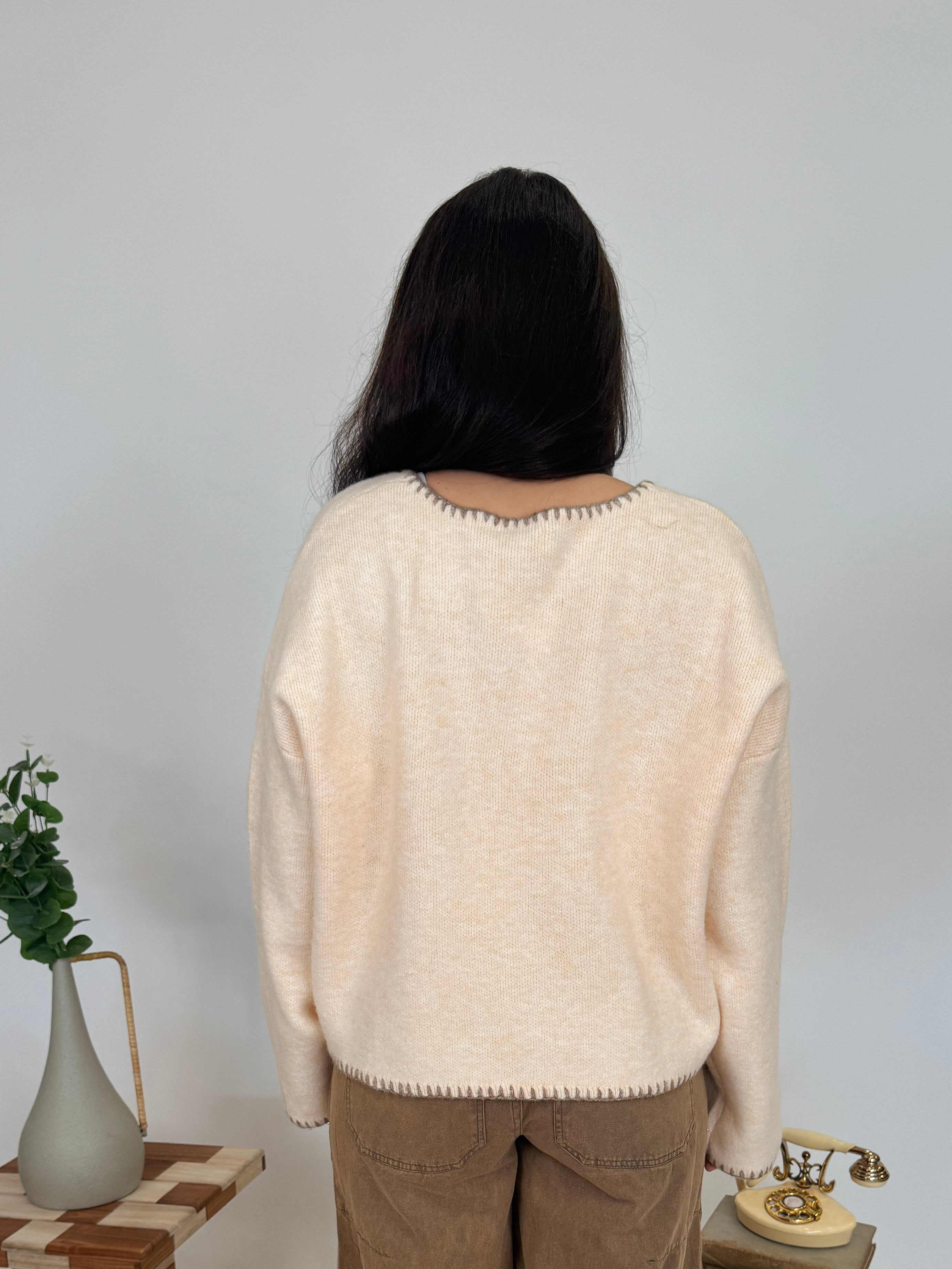 Person wearing a beige sweater and brown pants standing in a room with decorative elements.