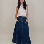 Belhaven Skirt in dark wash denim with a corset style lace up front, deep patch pockets, seamed panels, and a full sweeping maxi length
