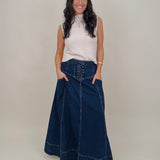 Belhaven Skirt in dark wash denim with a corset style lace up front, deep patch pockets, seamed panels, and a full sweeping maxi length