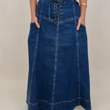 Belhaven Skirt in dark wash denim with a corset style lace up front, deep patch pockets, seamed panels, and a full sweeping maxi length