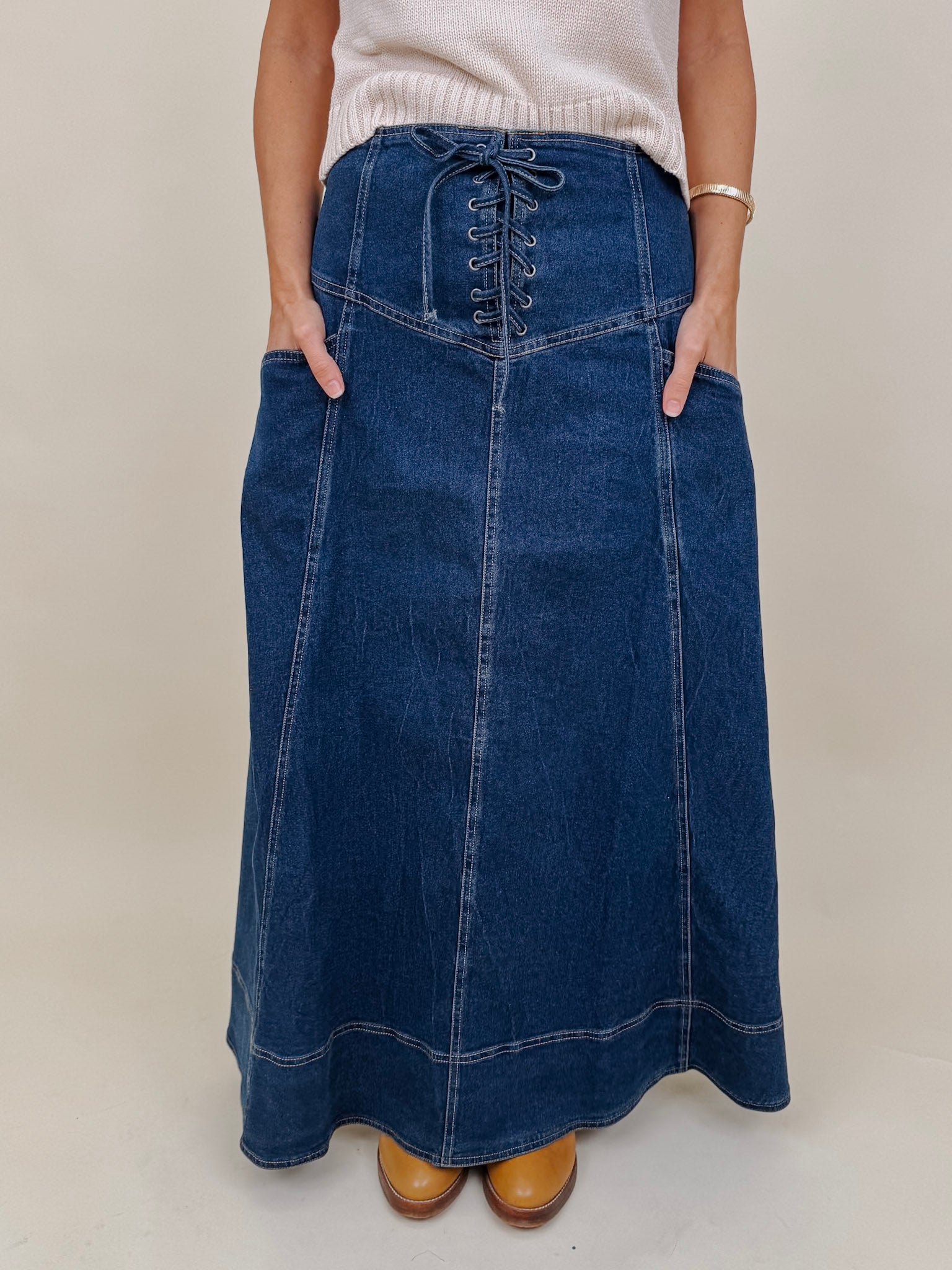 Belhaven Skirt in dark wash denim with a corset style lace up front, deep patch pockets, seamed panels, and a full sweeping maxi length