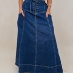 Belhaven Skirt in dark wash denim with a corset style lace up front, deep patch pockets, seamed panels, and a full sweeping maxi length
