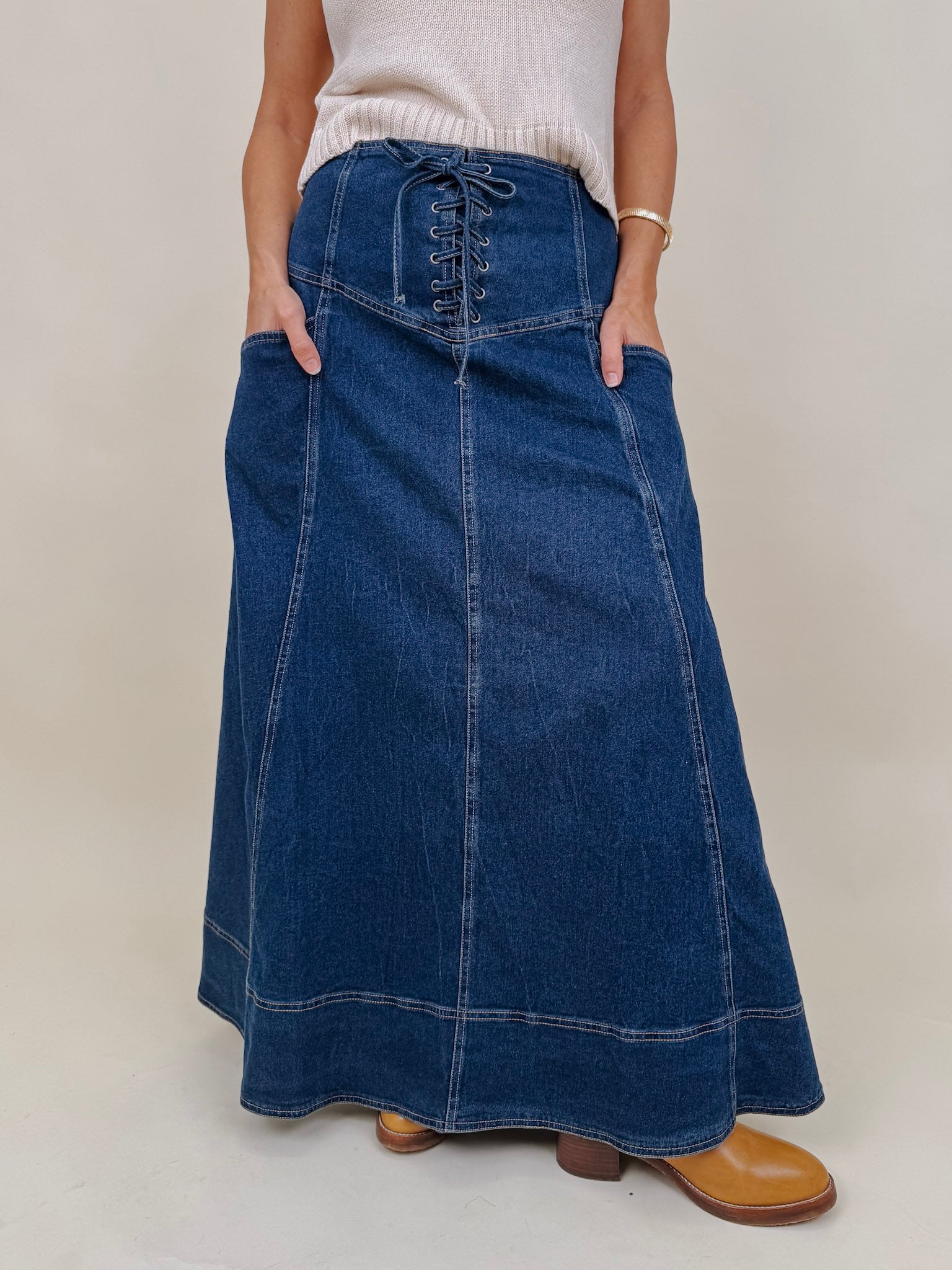 Belhaven Skirt in dark wash denim with a corset style lace up front, deep patch pockets, seamed panels, and a full sweeping maxi length