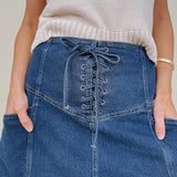 Belhaven Skirt in dark wash denim with a corset style lace up front, deep patch pockets, seamed panels, and a full sweeping maxi length