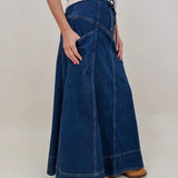 Belhaven Skirt in dark wash denim with a corset style lace up front, deep patch pockets, seamed panels, and a full sweeping maxi length