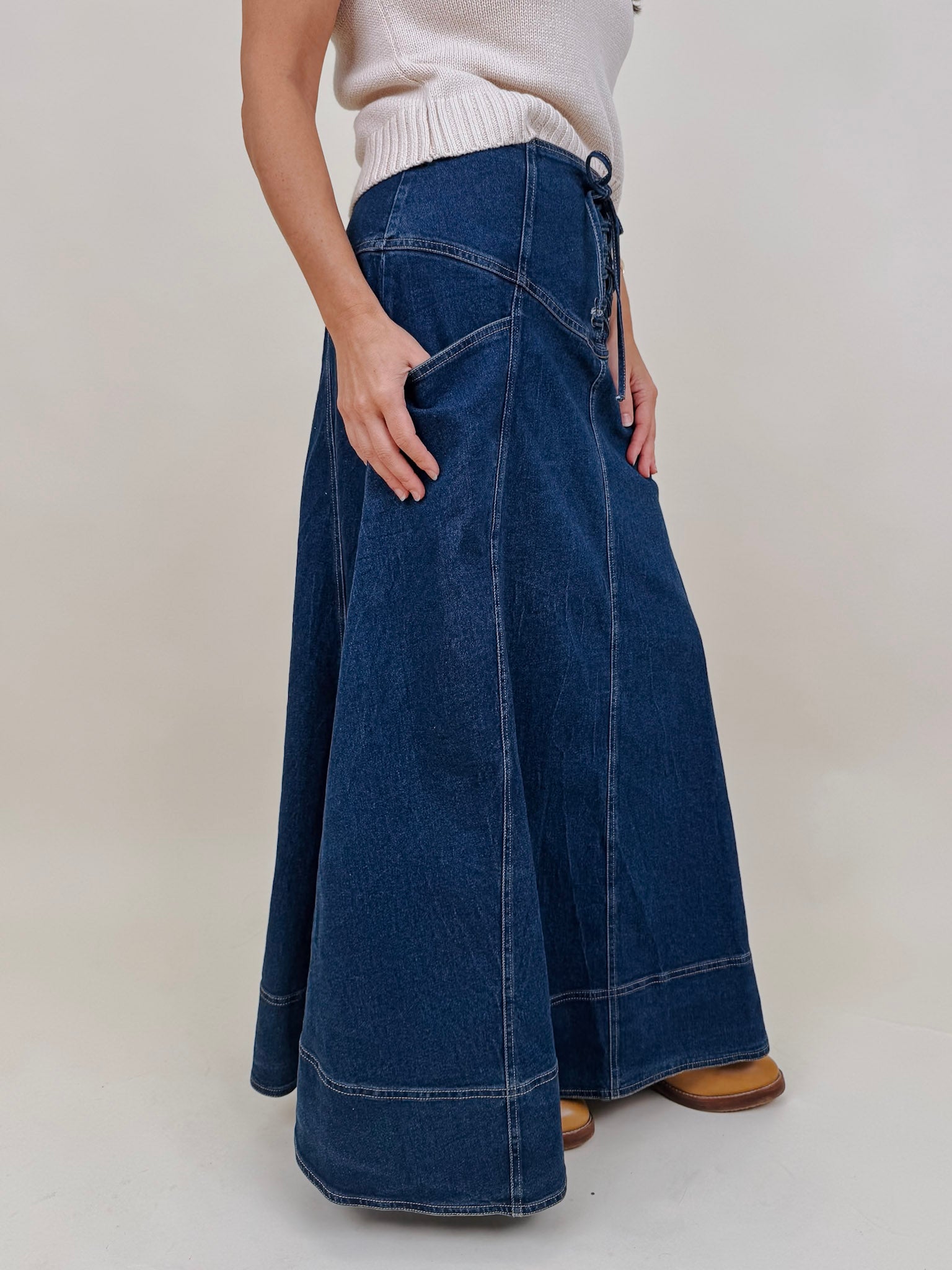 Belhaven Skirt in dark wash denim with a corset style lace up front, deep patch pockets, seamed panels, and a full sweeping maxi length