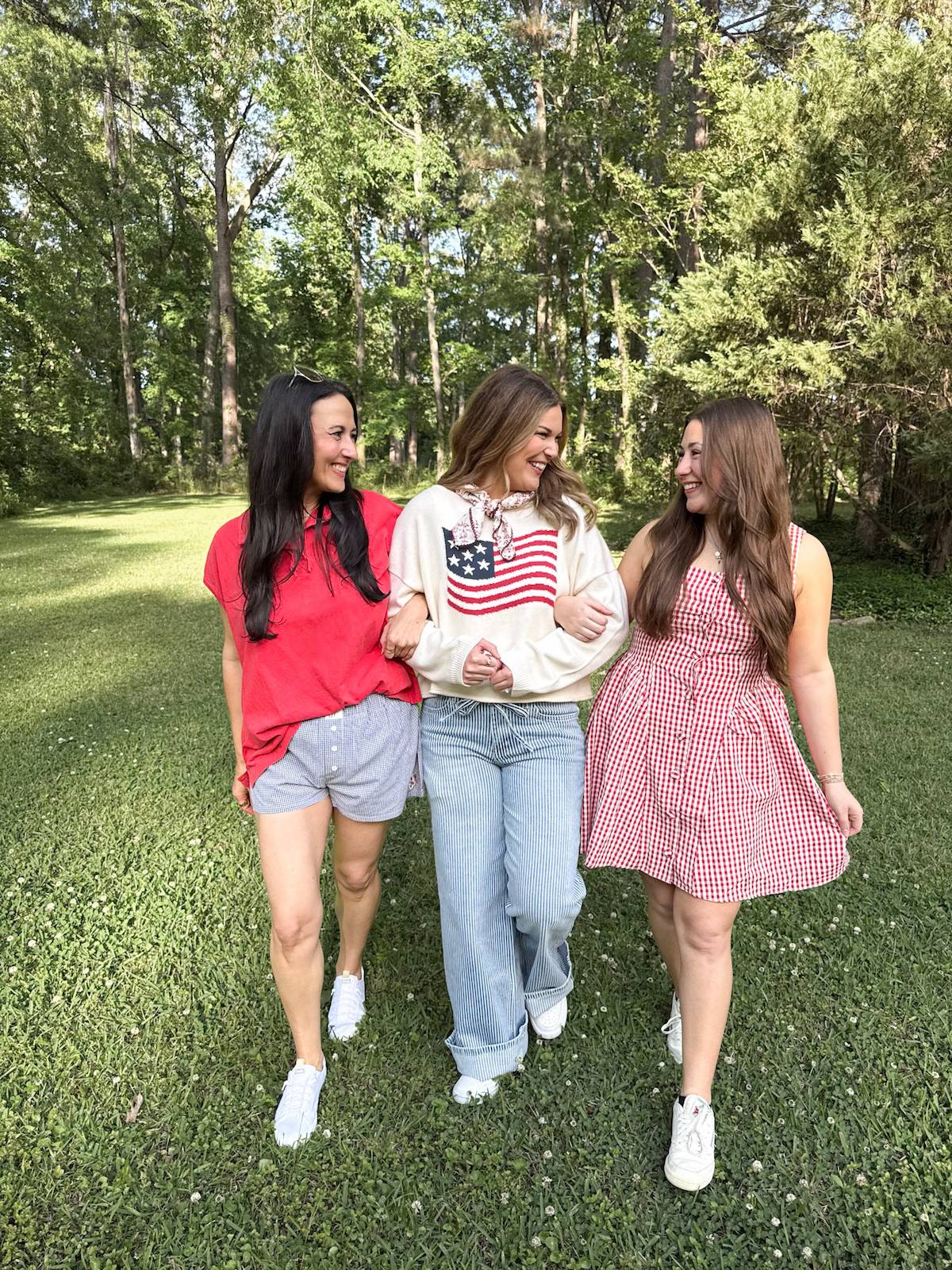 Three women walking together in a park with trees in the background
