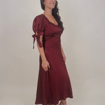 Katrina Midi Dress in burgundy crinkled satin with lace trim at the sweetheart neckline and empire waist, puff sleeves with bow ties, and a flowing bias cut midi skirt