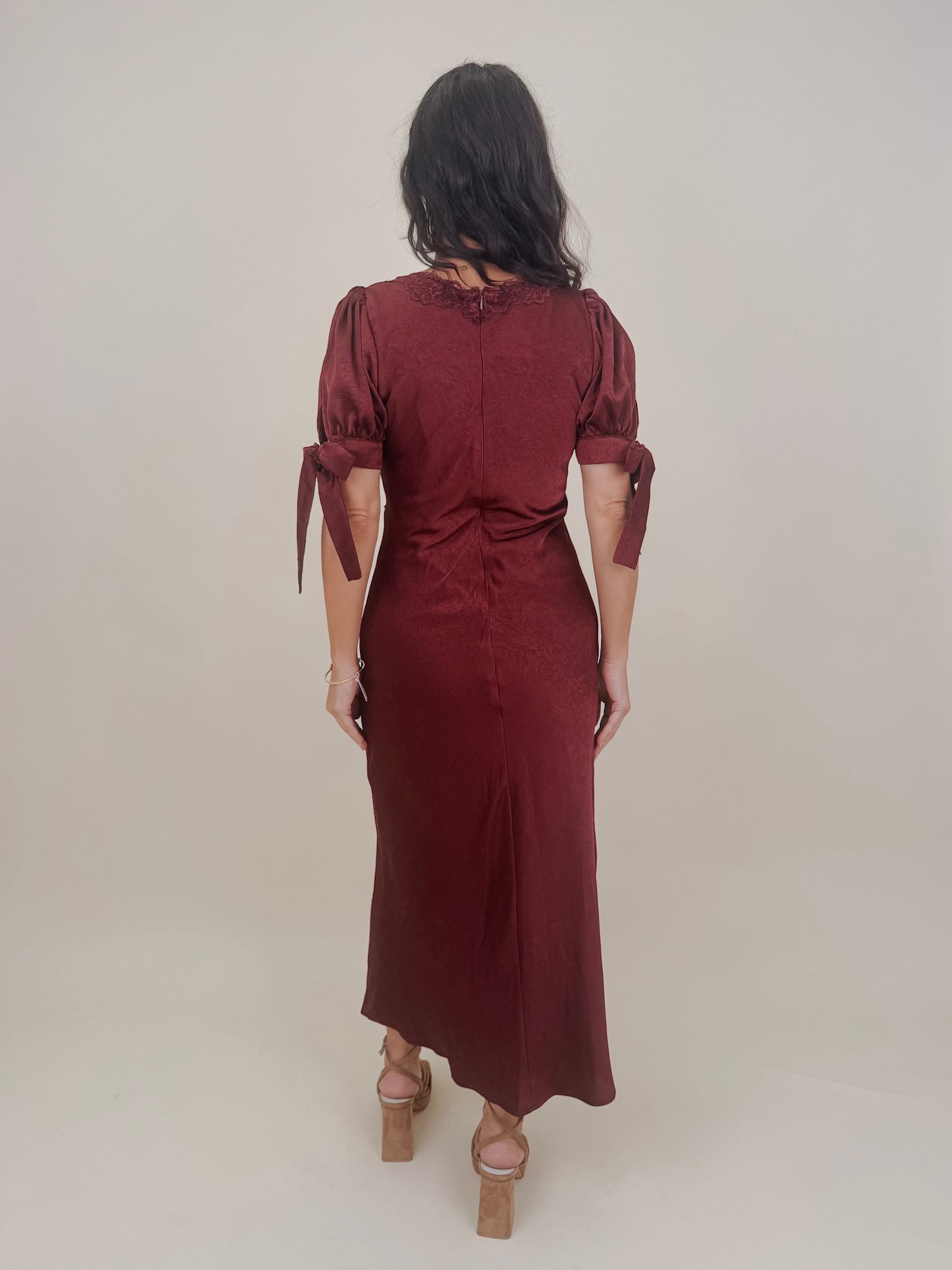 Katrina Midi Dress in burgundy crinkled satin with lace trim at the sweetheart neckline and empire waist, puff sleeves with bow ties, and a flowing bias cut midi skirt