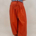 Magazine Street Pant in rust cotton with a smocked drawstring waist, gathered yoke, side pockets, and a full balloon leg