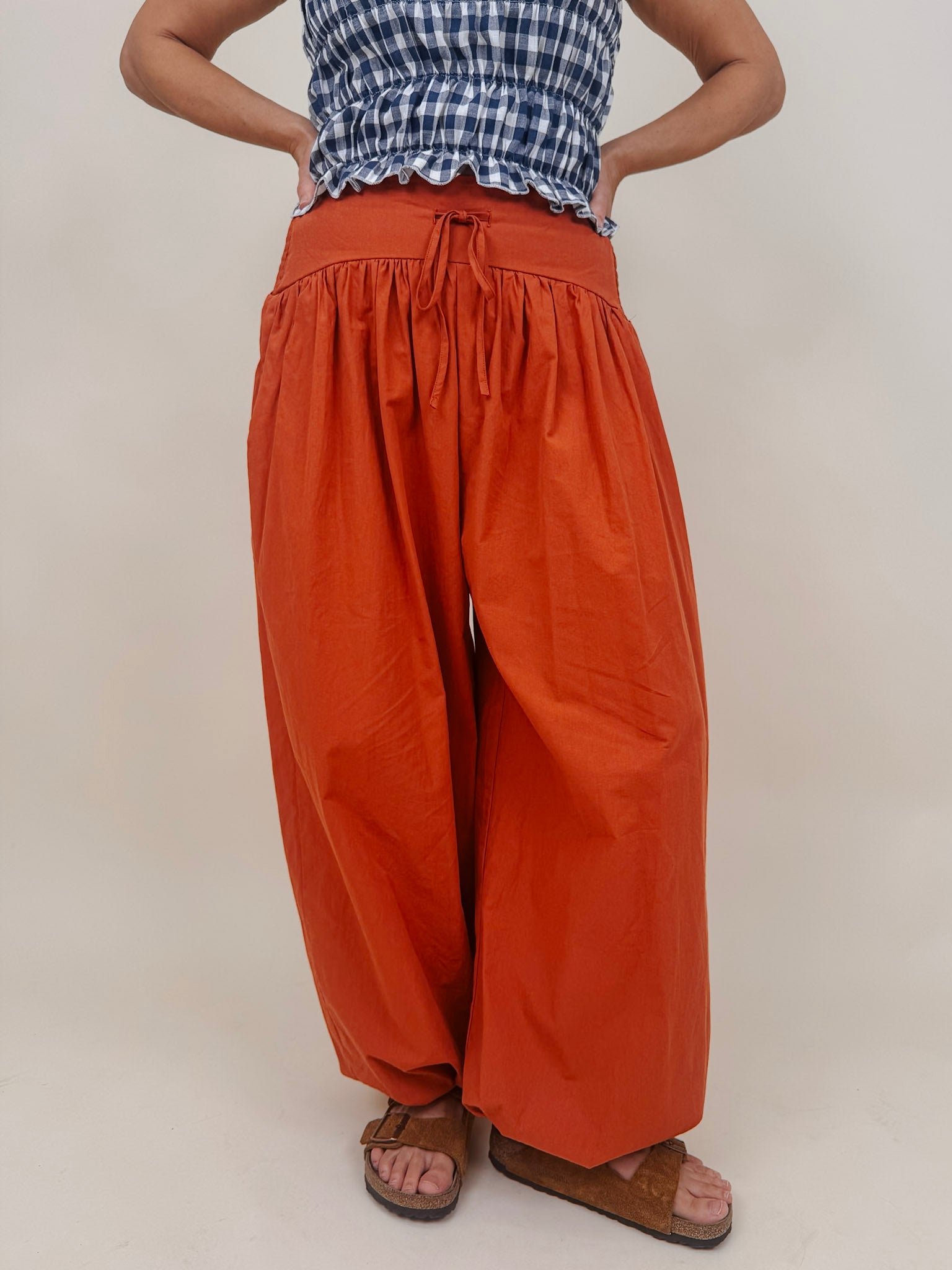 Magazine Street Pant in rust cotton with a smocked drawstring waist, gathered yoke, side pockets, and a full balloon leg