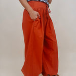 Magazine Street Pant in rust cotton with a smocked drawstring waist, gathered yoke, side pockets, and a full balloon leg