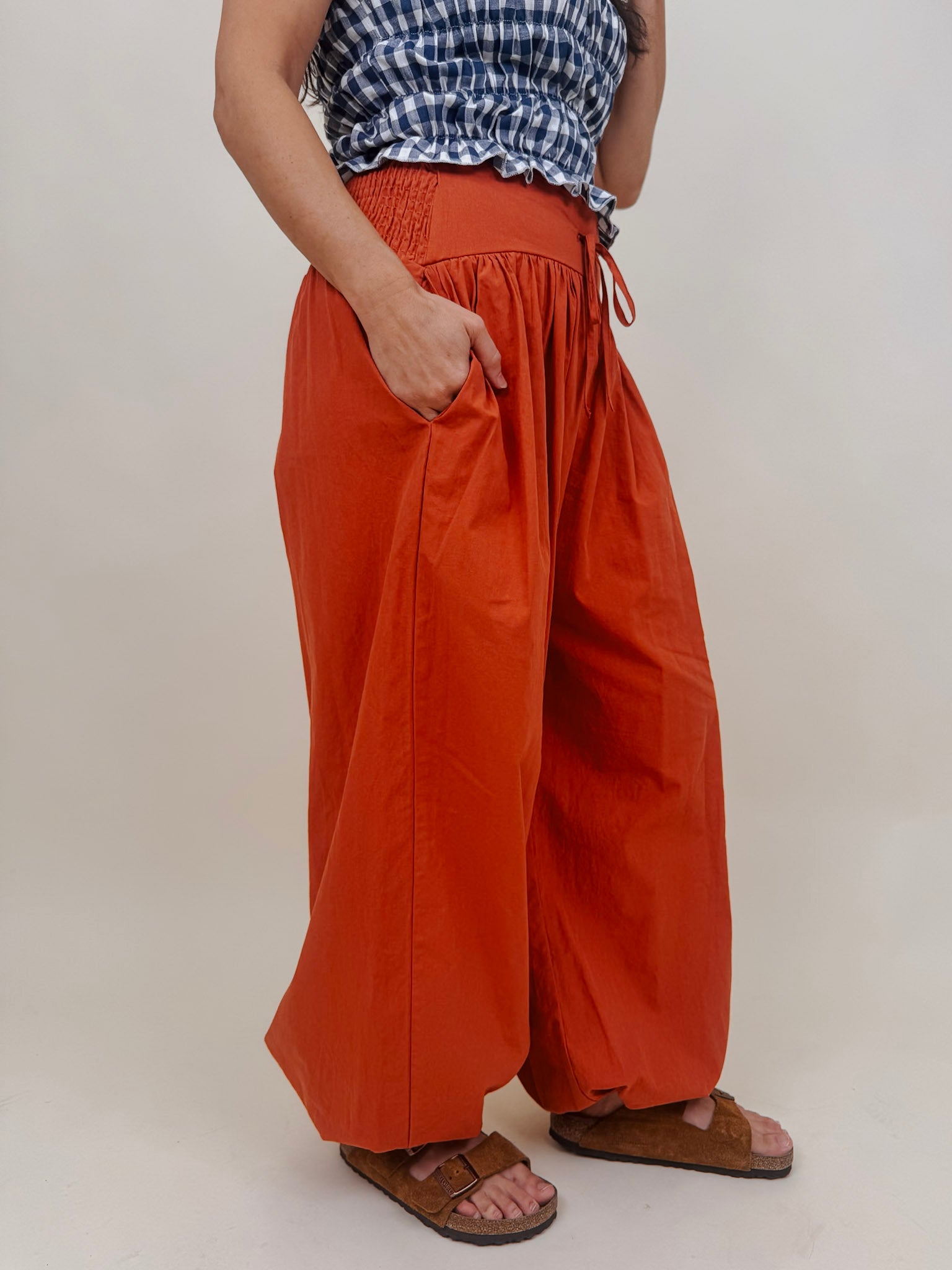 Magazine Street Pant in rust cotton with a smocked drawstring waist, gathered yoke, side pockets, and a full balloon leg