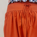 Magazine Street Pant in rust cotton with a smocked drawstring waist, gathered yoke, side pockets, and a full balloon leg