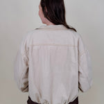 Pumpkin Patch Denim Jacket in soft beige with tortoise buttons over a hidden zip front, gathered shoulders, welt pockets, and an elastic bubble hem