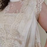 So Long London Blouse in champagne satin with eyelash lace panels, a mock neckline, cap sleeves, and a ruffled peplum hem with a ribbon tie back