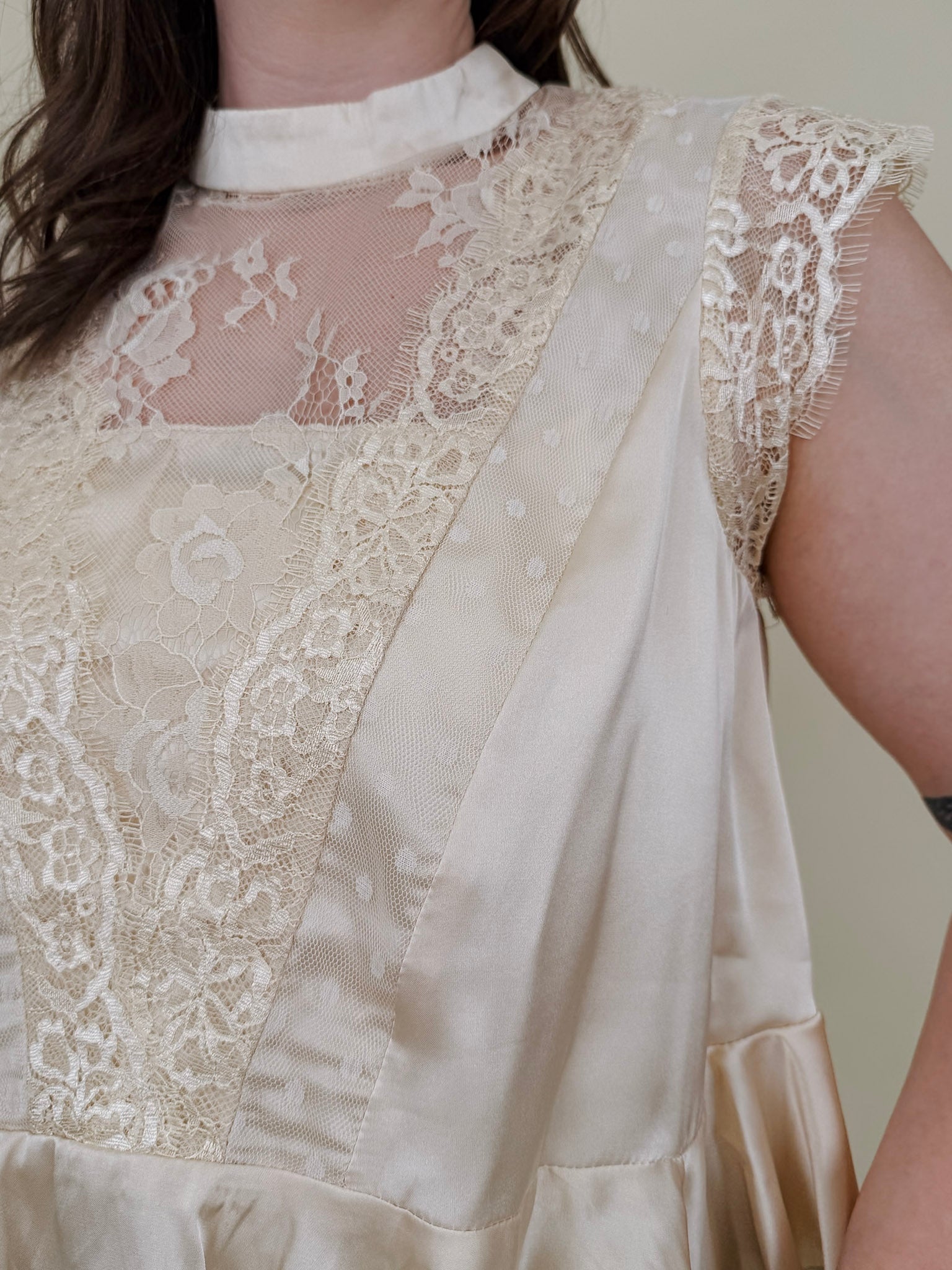 So Long London Blouse in champagne satin with eyelash lace panels, a mock neckline, cap sleeves, and a ruffled peplum hem with a ribbon tie back