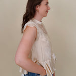 So Long London Blouse in champagne satin with eyelash lace panels, a mock neckline, cap sleeves, and a ruffled peplum hem with a ribbon tie back