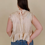 So Long London Blouse in champagne satin with eyelash lace panels, a mock neckline, cap sleeves, and a ruffled peplum hem with a ribbon tie back