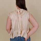 So Long London Blouse in champagne satin with eyelash lace panels, a mock neckline, cap sleeves, and a ruffled peplum hem with a ribbon tie back