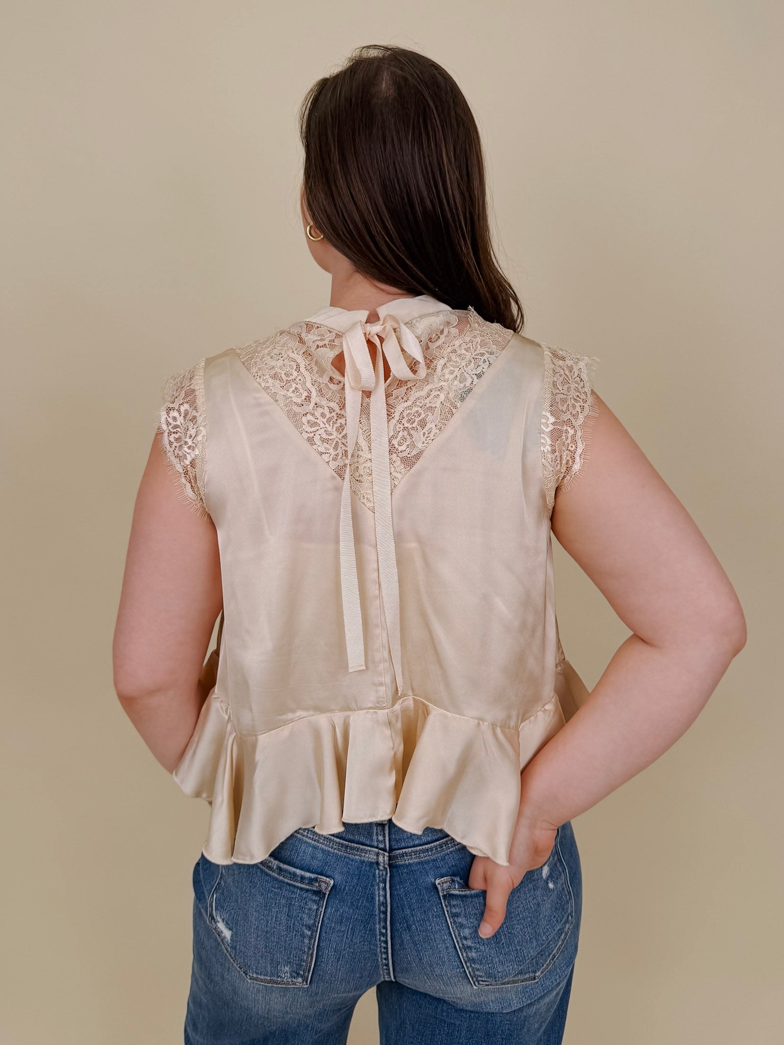 So Long London Blouse in champagne satin with eyelash lace panels, a mock neckline, cap sleeves, and a ruffled peplum hem with a ribbon tie back