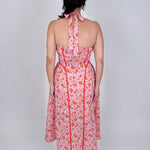 Tara Dress in pink ditsy floral print with red contrast piping, halter V neckline, fitted bodice, and full gathered midi skirt