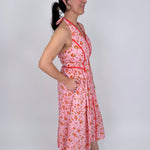 Tara Dress in pink ditsy floral print with red contrast piping, halter V neckline, fitted bodice, and full gathered midi skirt