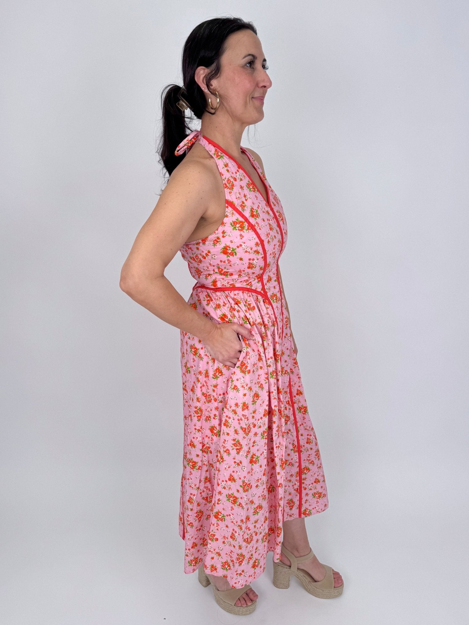 Tara Dress in pink ditsy floral print with red contrast piping, halter V neckline, fitted bodice, and full gathered midi skirt