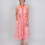 Tara Dress in pink ditsy floral print with red contrast piping, halter V neckline, fitted bodice, and full gathered midi skirt